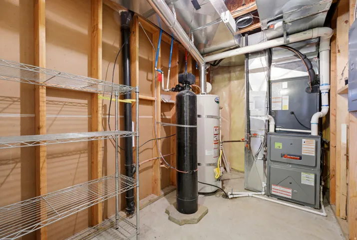 Utility room featuring a furnace, water heater, water treatment system, and exposed wood framing
