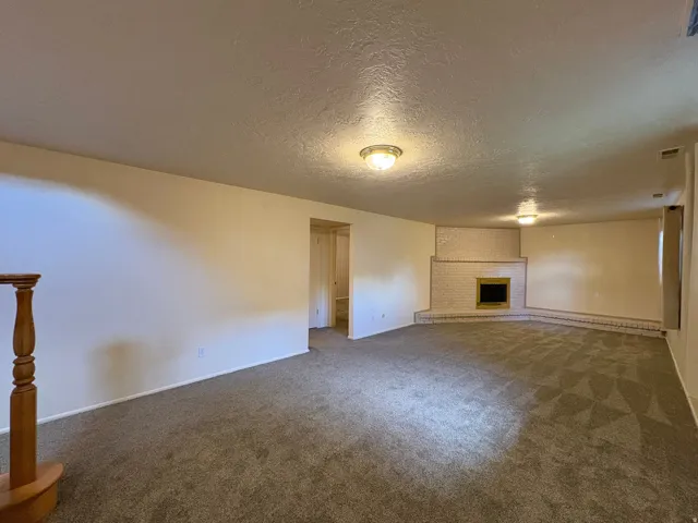Spacious room featuring neutral carpet flooring, a corner brick fireplace with a hearth, and light-colored walls