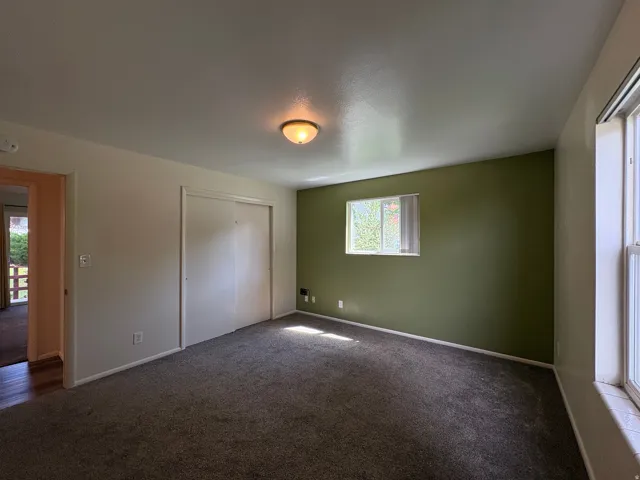 Carpeted room featuring a single window with blinds, a contrasting accent wall, a flush-mount ceiling light fixture, and a closet with sliding doors