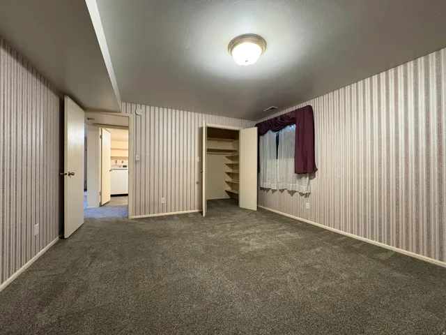 Carpeted room featuring striped wallpaper, a flush-mount ceiling light fixture, and a built-in closet with shelving