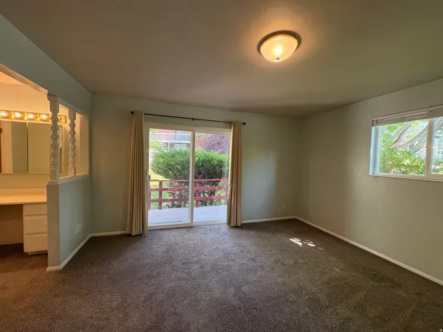 Carpeted room featuring a ceiling-mounted light fixture, sliding glass doors to an outdoor deck, and a single-pane window