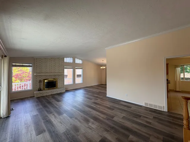 Spacious living area featuring contemporary wood-finish flooring, a white brick fireplace with a brass-trimmed insert, and large windows with transom architectural details