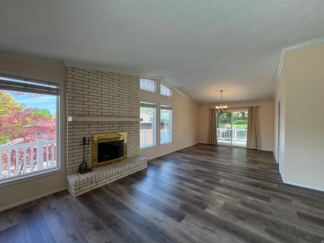 Spacious living area featuring plank wood-finish flooring and a brick-faced fireplace with a brass-trimmed insert