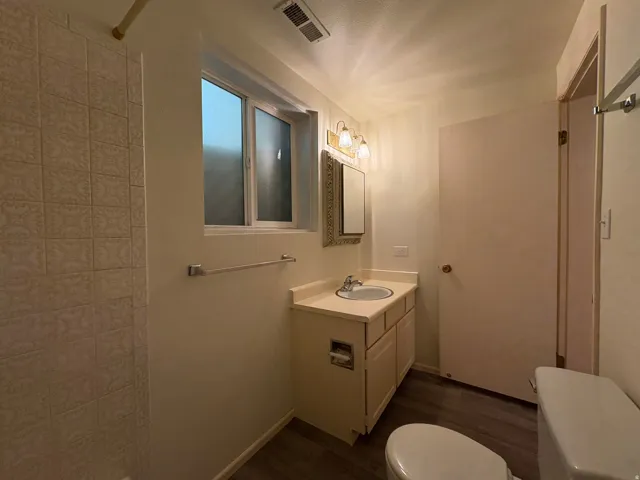 Bathroom featuring a single vanity with an integrated sink, wood-finish flooring, a window with frosted panes, and a tiled shower surround
