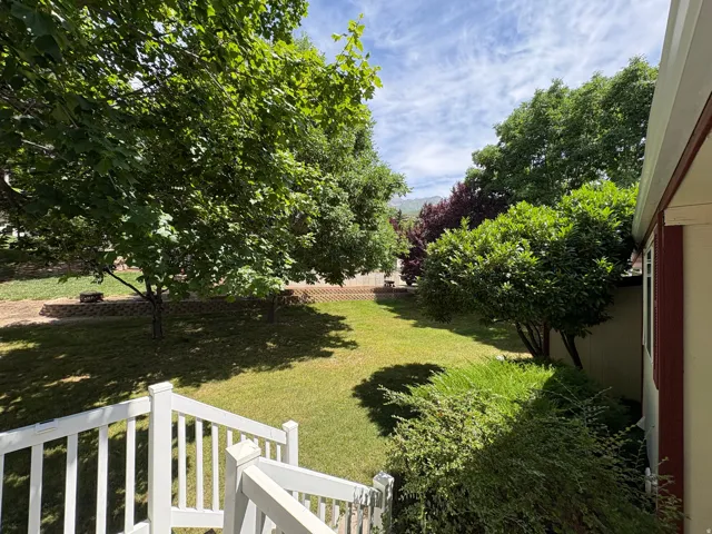 Expansive backyard featuring a manicured lawn, mature trees, tiered landscaping with stone retaining walls, and surrounding greenery