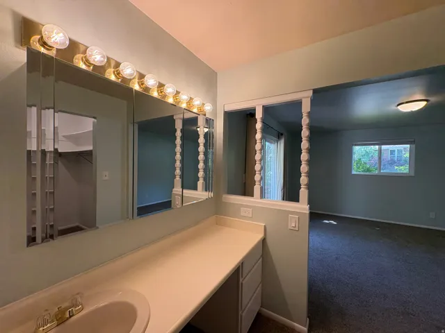 Vanity area featuring a built-in countertop with an integrated sink, tri-fold mirror, and overhead vanity lighting
