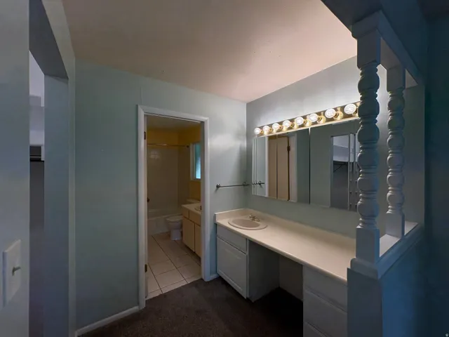 Vanity area featuring a built-in countertop with an integrated sink, white cabinetry, and a full-width mirror with overhead lighting