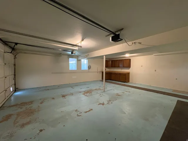Spacious garage featuring an automatic overhead door, built-in cabinetry with counter space, two windows for natural light, and ceiling-mounted fluorescent lighting