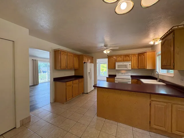 Kitchen featuring tile flooring, wood cabinetry, built-in white appliances, a double-basin sink, and a peninsula countertop