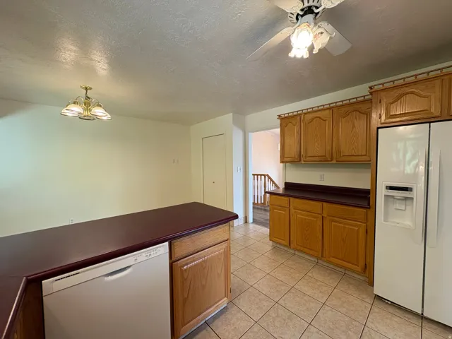 Kitchen featuring wood-finish cabinetry, a central island with a built-in dishwasher, and tile flooring