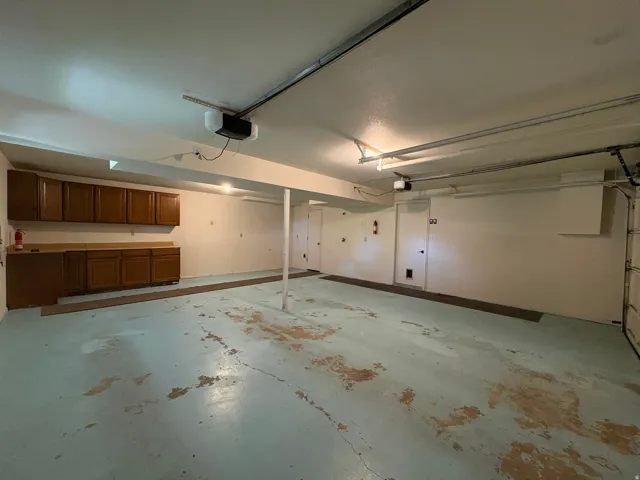 Spacious garage featuring extensive built-in cabinetry and countertops, a durable painted concrete floor, overhead lighting, and an automatic garage door opener