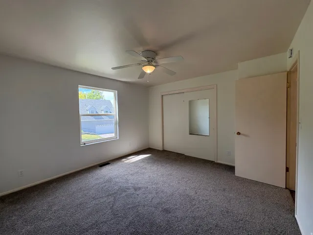 Carpeted room featuring a ceiling fan with integrated lighting, a double-pane window, and a sliding closet door with a mirrored panel