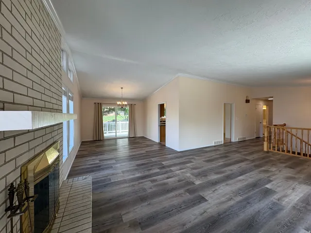Spacious interior featuring wide plank wood-finish flooring, a brick fireplace with a white mantel, and ample natural light from multiple windows