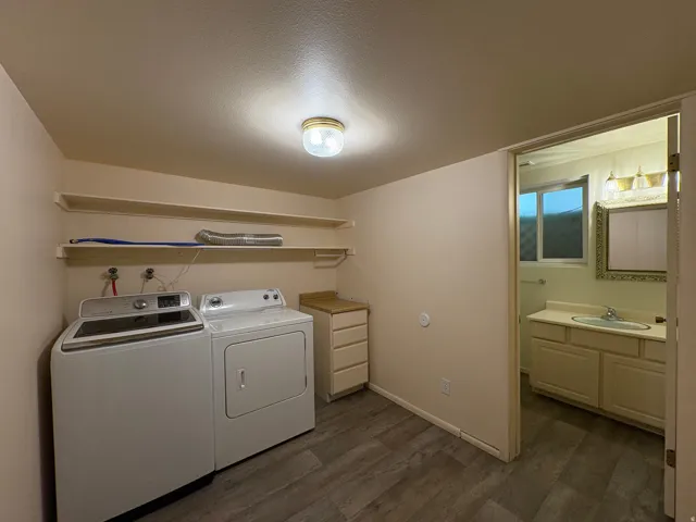 Dedicated laundry area featuring wood-finish flooring, built-in shelving, and an adjacent bathroom with a vanity and mirror