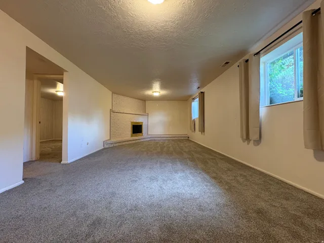 Spacious carpeted room featuring a white brick fireplace with a dark insert, multiple windows, and recessed lighting