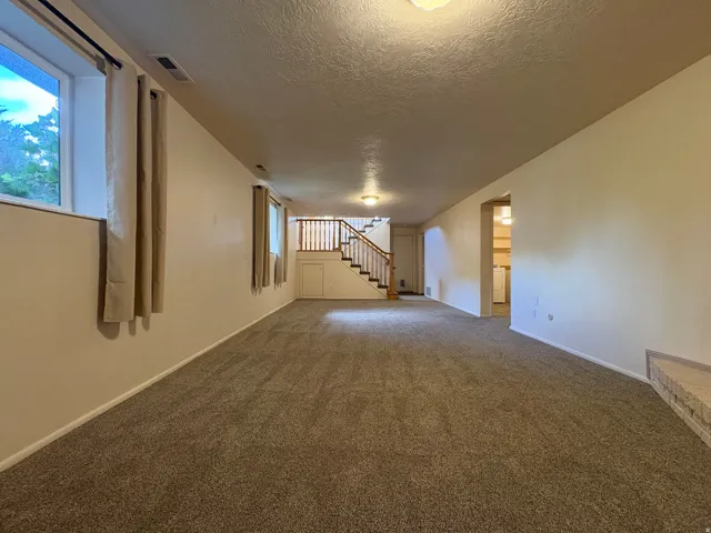 Spacious room featuring neutral carpet flooring, recessed windows, a wood staircase with white risers, and a built-in storage cabinet under the stairs