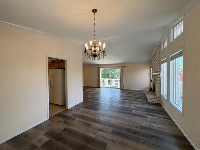 Spacious living area featuring wood-finish flooring, a decorative chandelier, and a brick fireplace