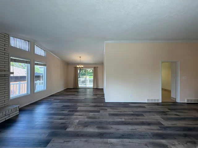 Spacious interior featuring wood-finish flooring, a white brick fireplace, multiple large windows, and crown molding