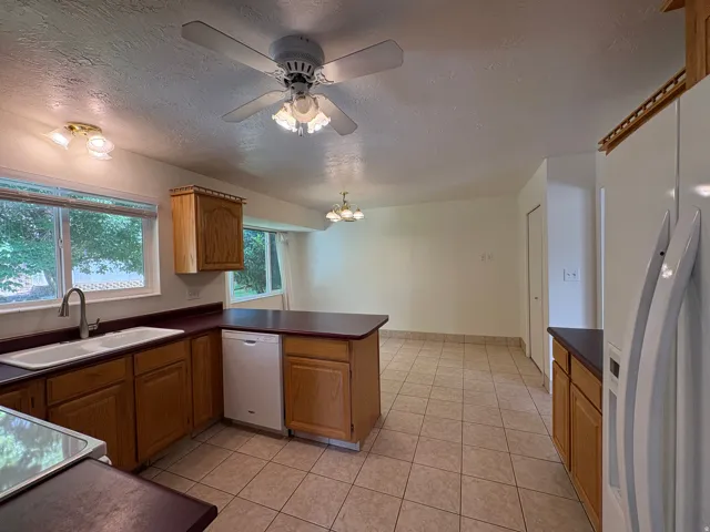 Kitchen featuring wood cabinetry, a double basin sink with a gooseneck faucet, a white dishwasher, and tiled flooring