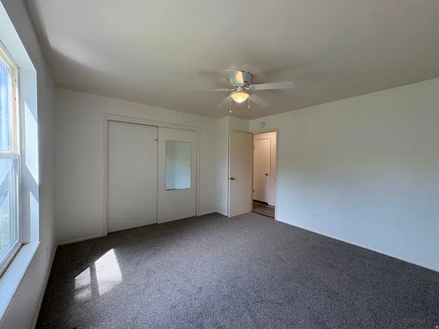 Carpeted room featuring a ceiling fan with integrated lighting, sliding closet doors with one mirrored panel, and a large window
