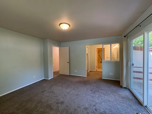 Carpeted room featuring a ceiling-mounted light fixture, light blue wall paint, white trim, and sliding glass patio doors opening to an exterior deck area