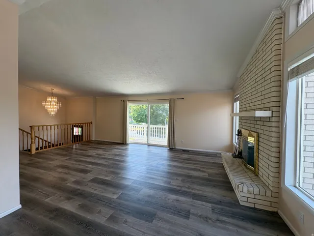 Spacious living area featuring wood-finish flooring, a light brick fireplace with a hearth and mantel, and large windows