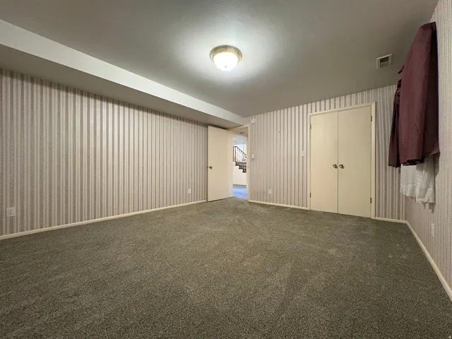 Carpeted room featuring striped wallpaper, a flush-mount ceiling light fixture, and a built-in double-door closet