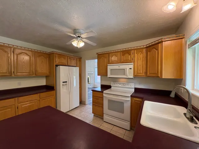 Kitchen featuring wood-finish cabinetry, white appliances, and a ceiling fan with integrated lighting