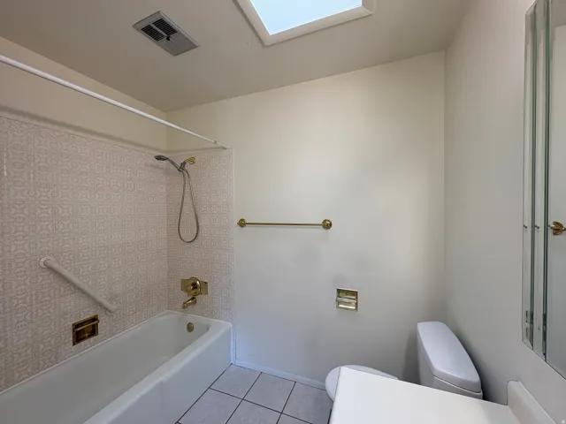 Full bathroom with a tub/shower combination, patterned wall tile, skylight, and white floor tile