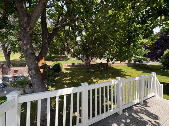 Expansive outdoor space featuring a composite deck with white railings, mature trees providing natural shade, a verdant lawn, and a brick retaining wall