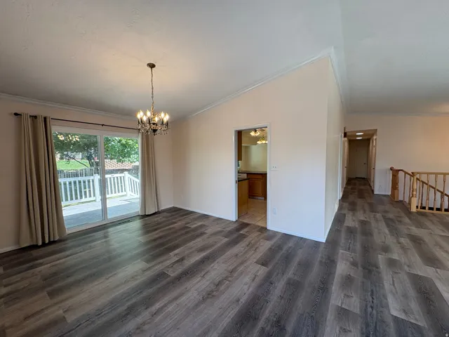 Spacious room featuring wood-finish flooring, a contemporary chandelier, and direct access to an outdoor deck through a large sliding glass door