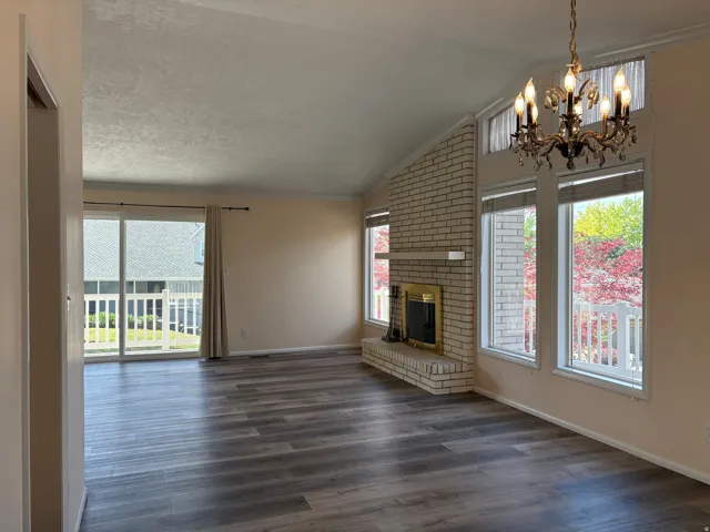 Vaulted ceiling living area featuring wood-finish flooring, a brick fireplace with a golden firebox, multiple windows, and a sliding glass door