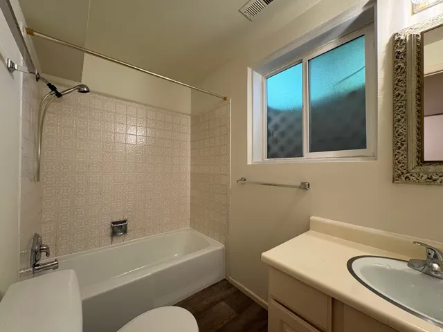 Bathroom featuring a white bathtub with patterned tile surround, a built-in vanity with integrated sink, and wood-finish flooring