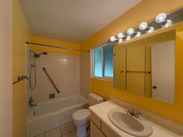 Bathroom featuring a single vanity with an integrated sink, a large mirrored medicine cabinet, a vanity light fixture, and a bathtub with a tiled surround