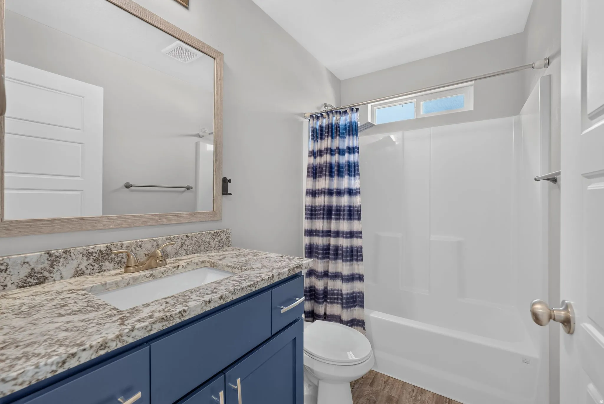 Bathroom featuring a blue shaker-style vanity with chrome hardware, a light-toned granite countertop with an undermount sink, and a brushed brass faucet