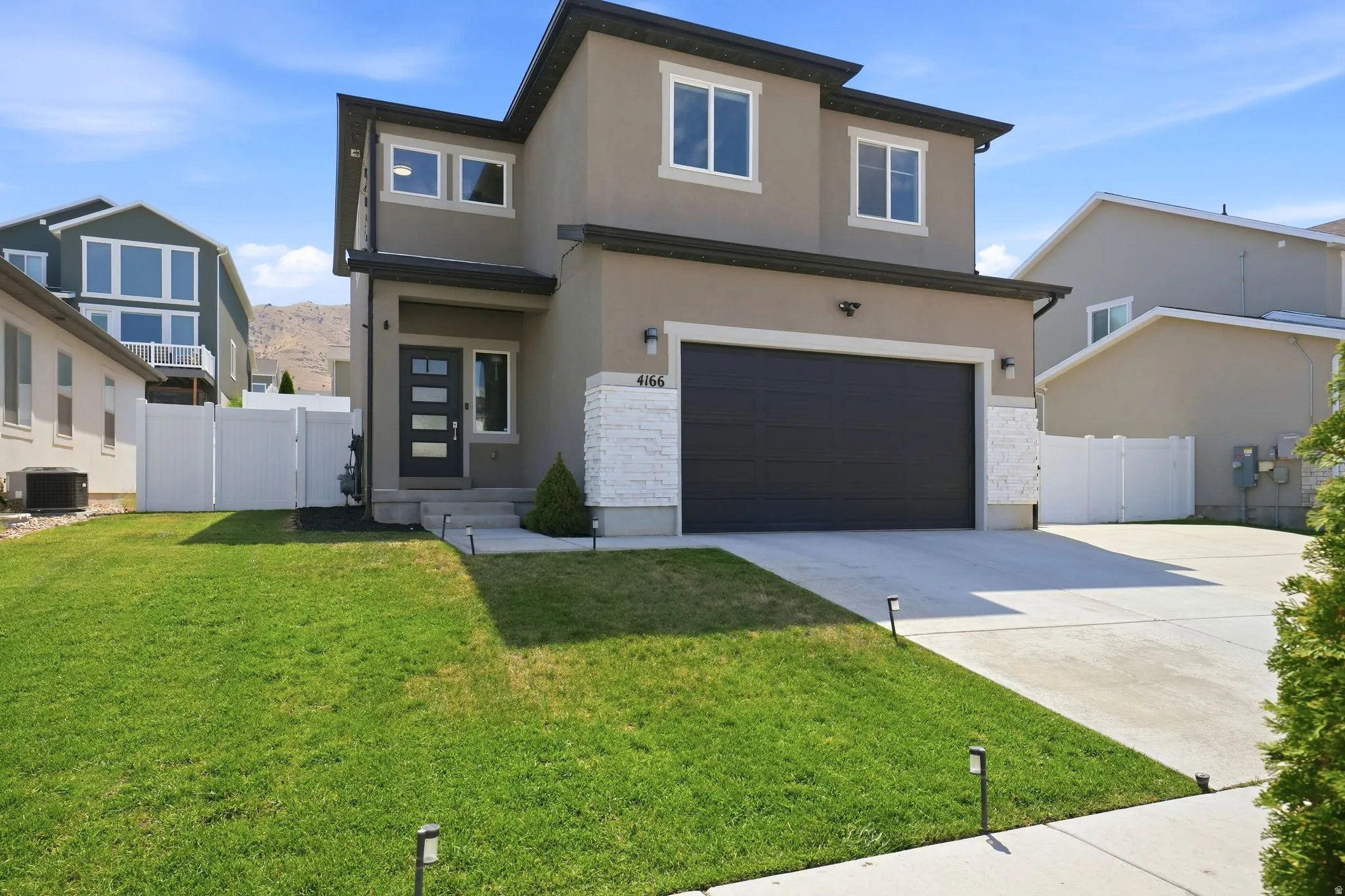 Contemporary stucco exterior with a dark garage door, white stone accent, and a paved driveway