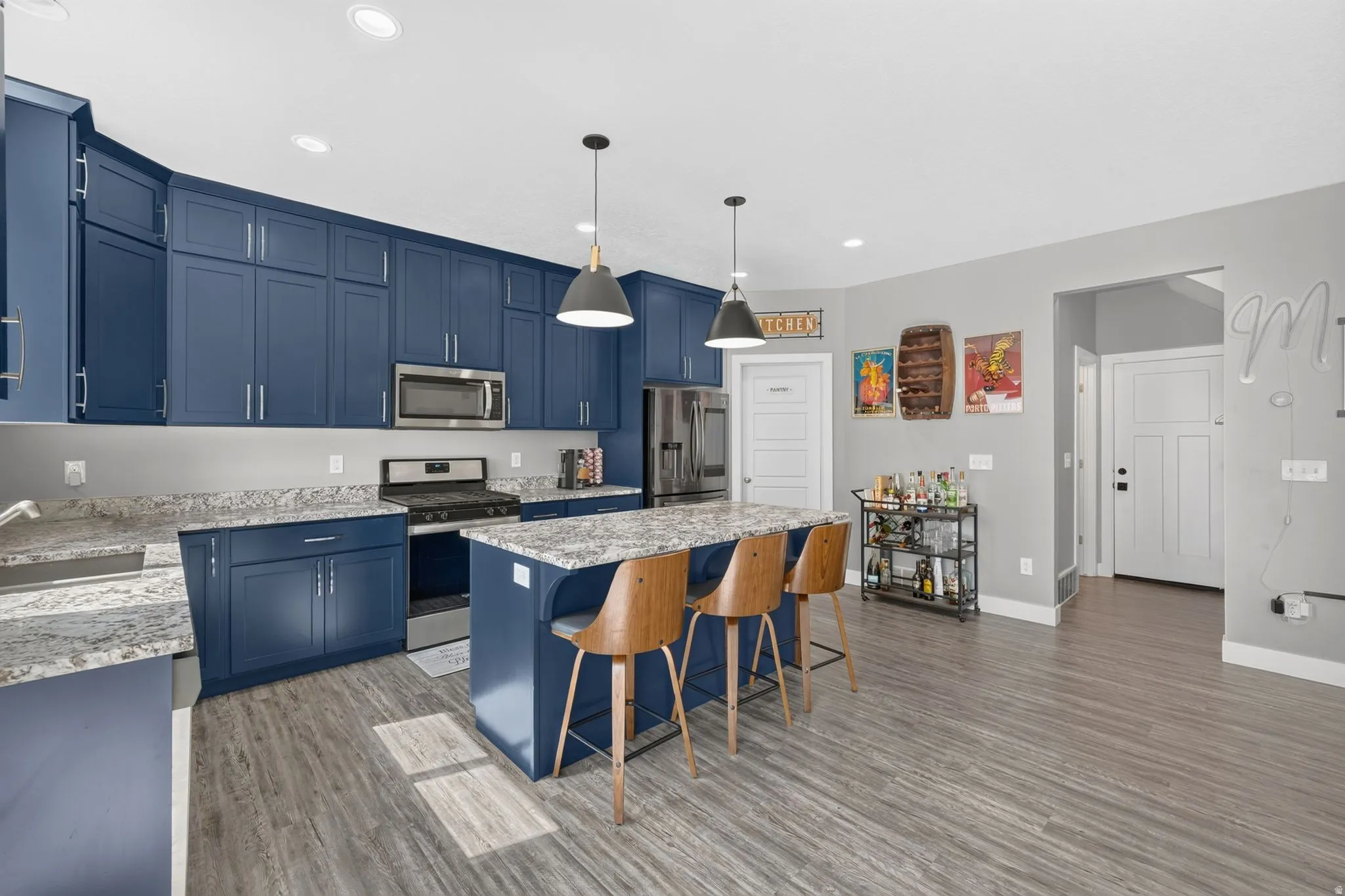 Spacious kitchen featuring deep blue cabinetry, granite countertops, stainless steel appliances, a center island with seating, and wood-finish flooring