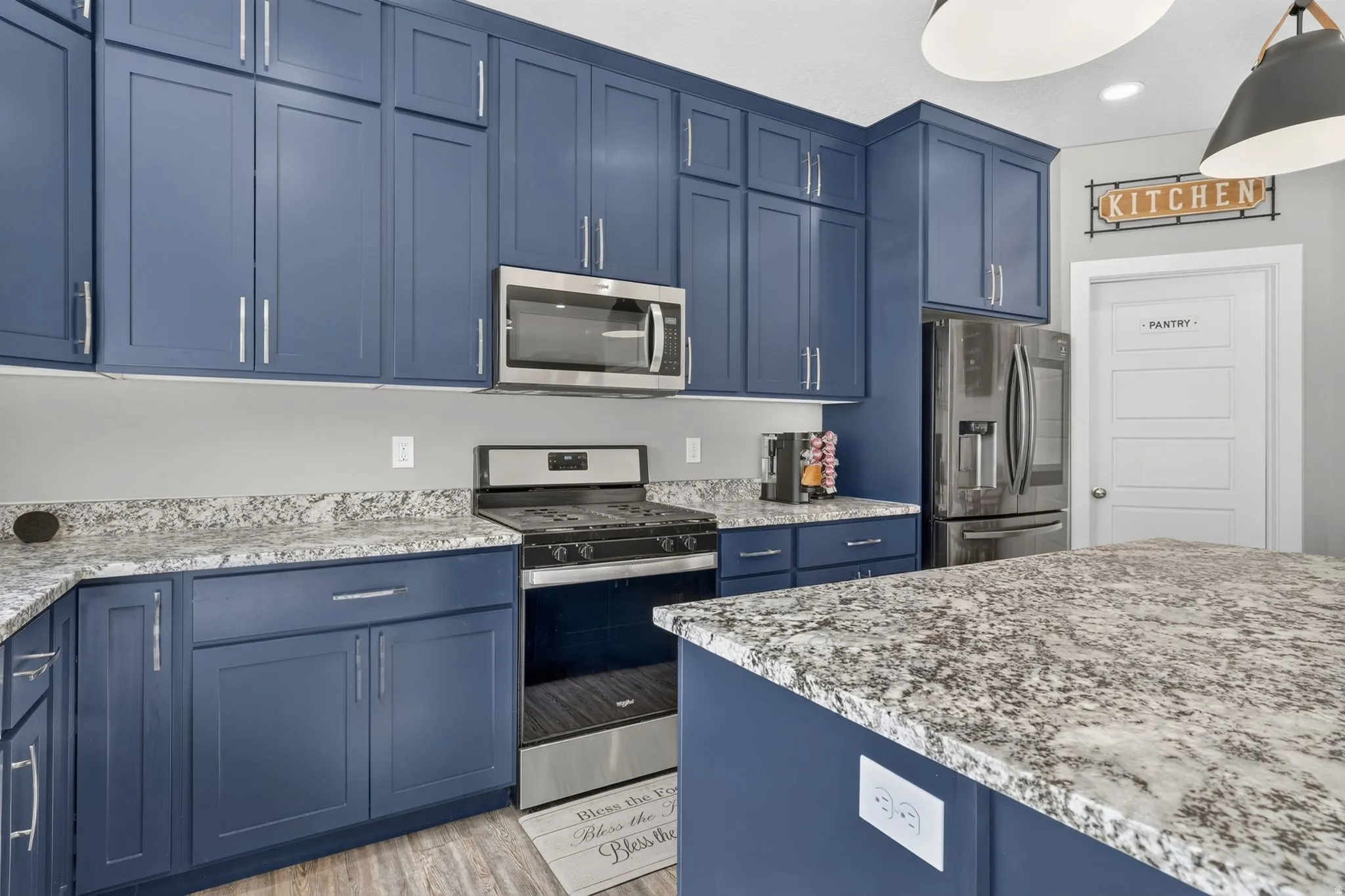 Modern kitchen featuring blue cabinetry, light-toned countertops, stainless steel appliances, and a central island