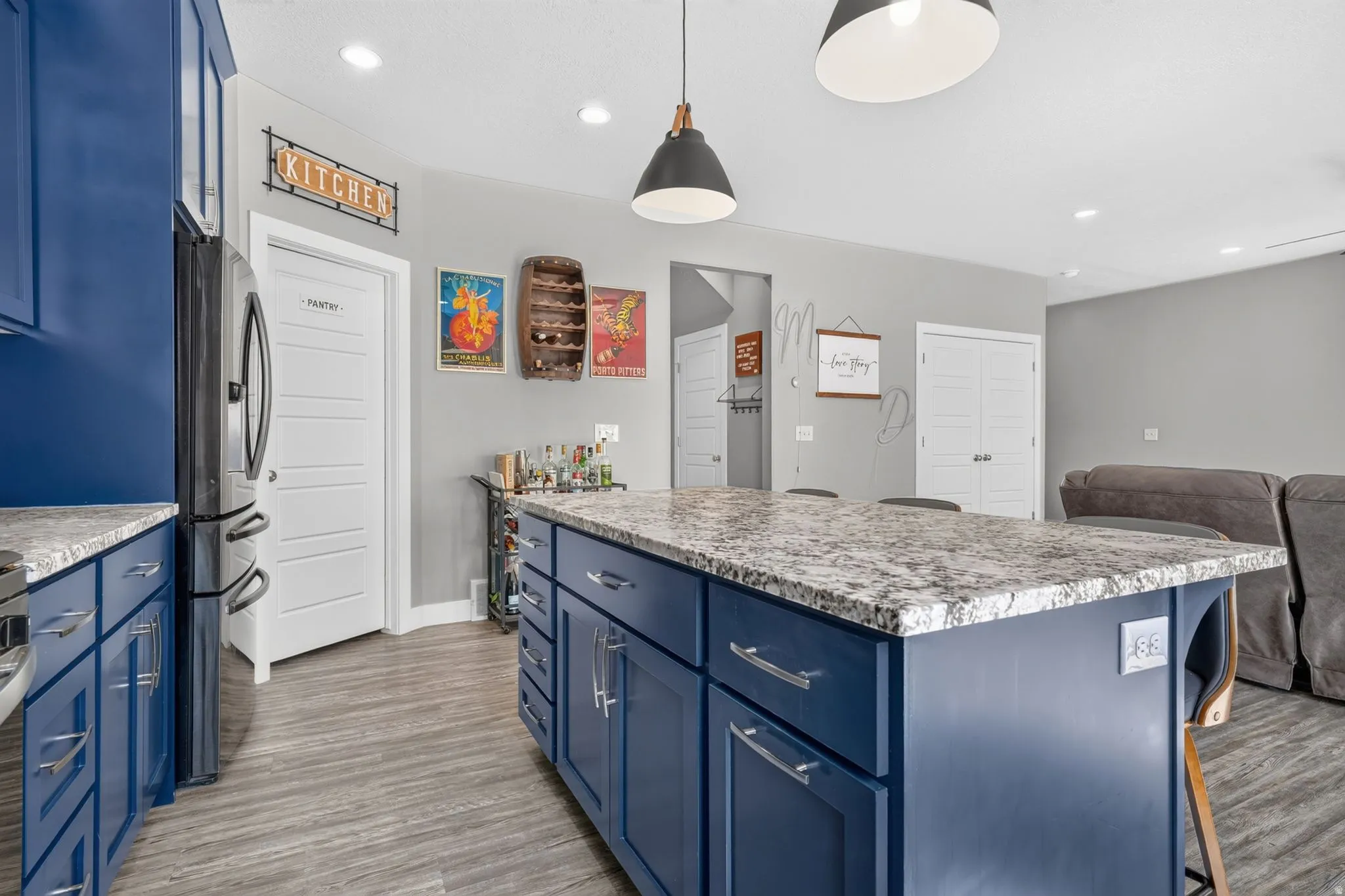 Open-concept kitchen featuring a spacious island with a stone-finish countertop, dark blue cabinetry, recessed lighting, and wood-finish flooring