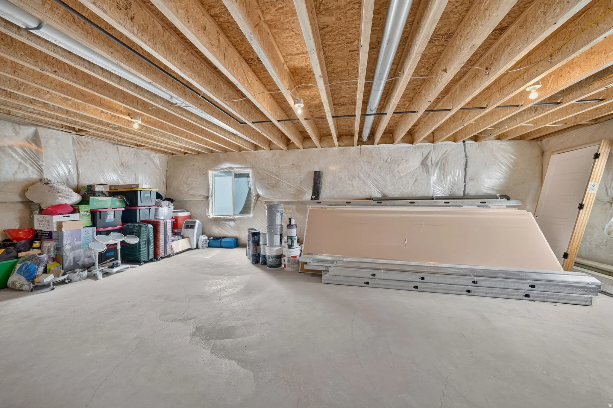 Unfinished basement space featuring exposed wood joists, concrete flooring, and a small window