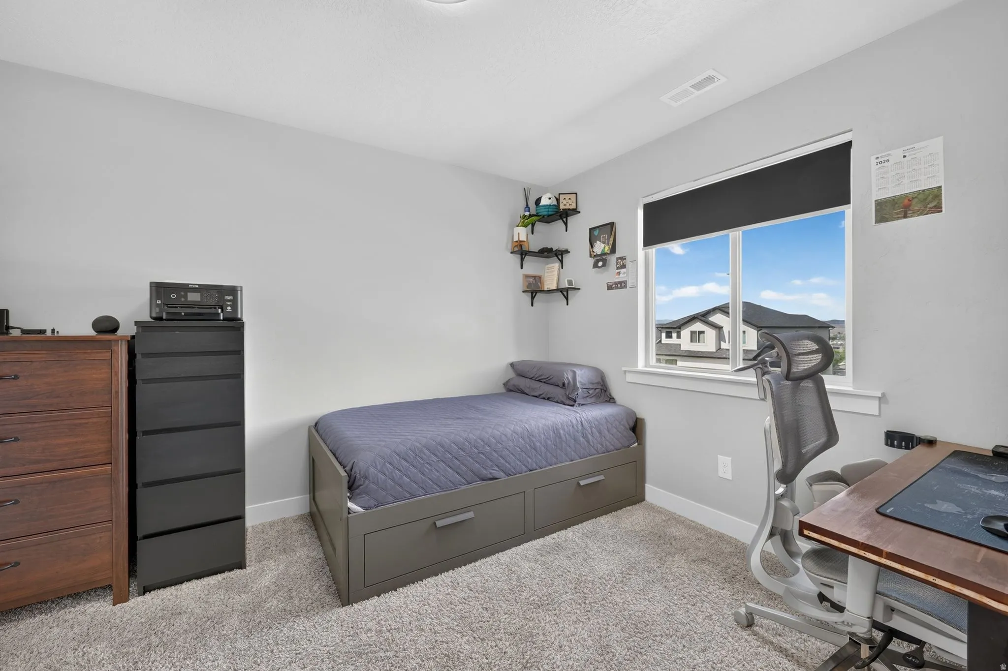 Well-lit room featuring light gray walls, plush carpet flooring, a large window with white trim, and a ceiling light fixture