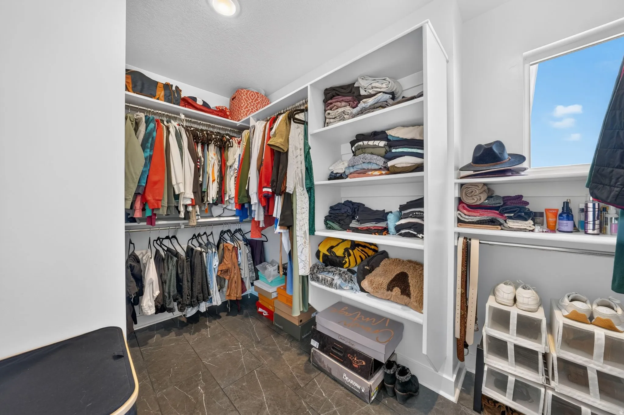 Spacious walk-in closet featuring built-in shelving, multiple hanging rods, recessed lighting, a window, and dark tile flooring