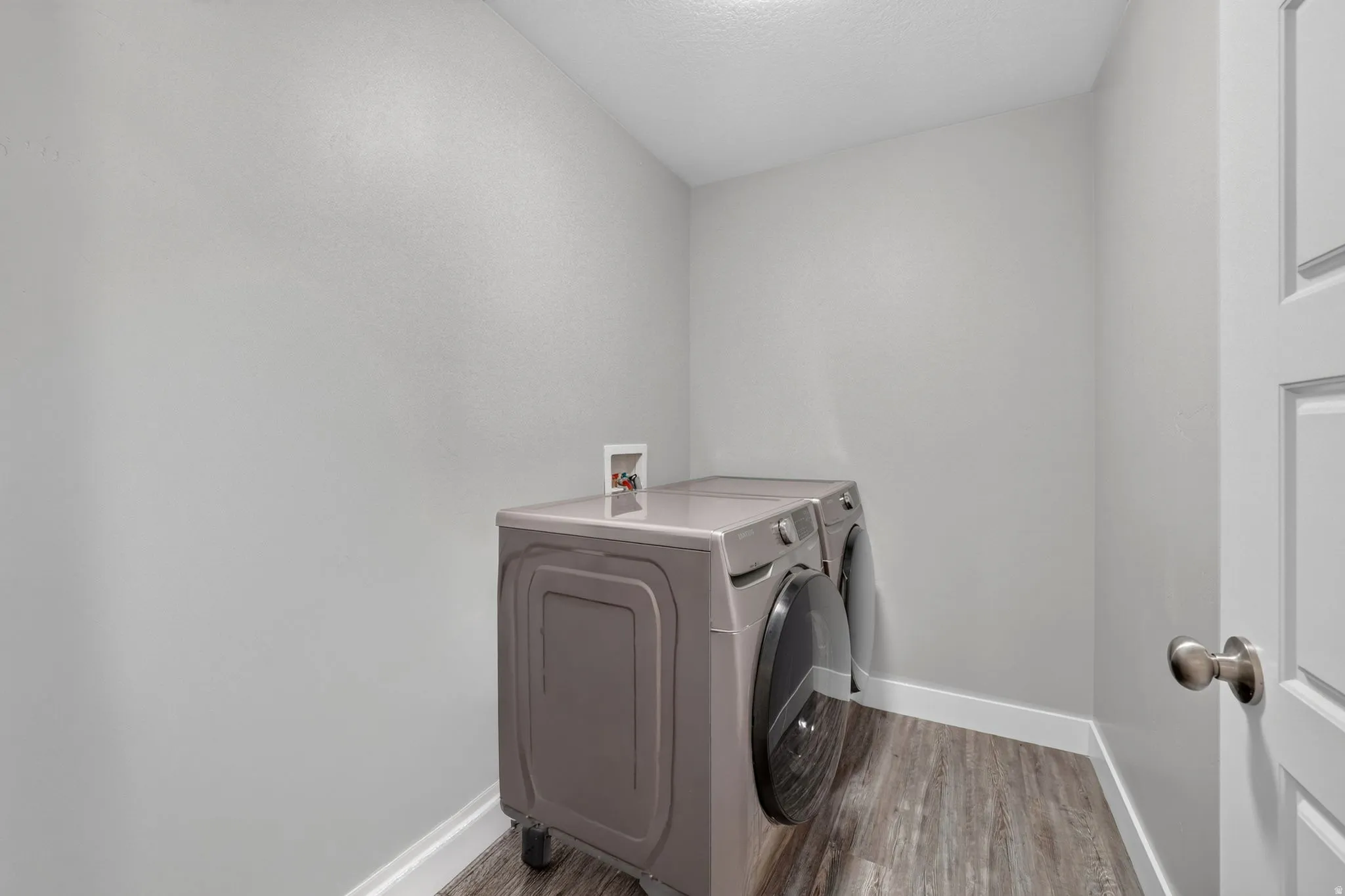Dedicated laundry area with wood-finish flooring, light grey walls, and white baseboards