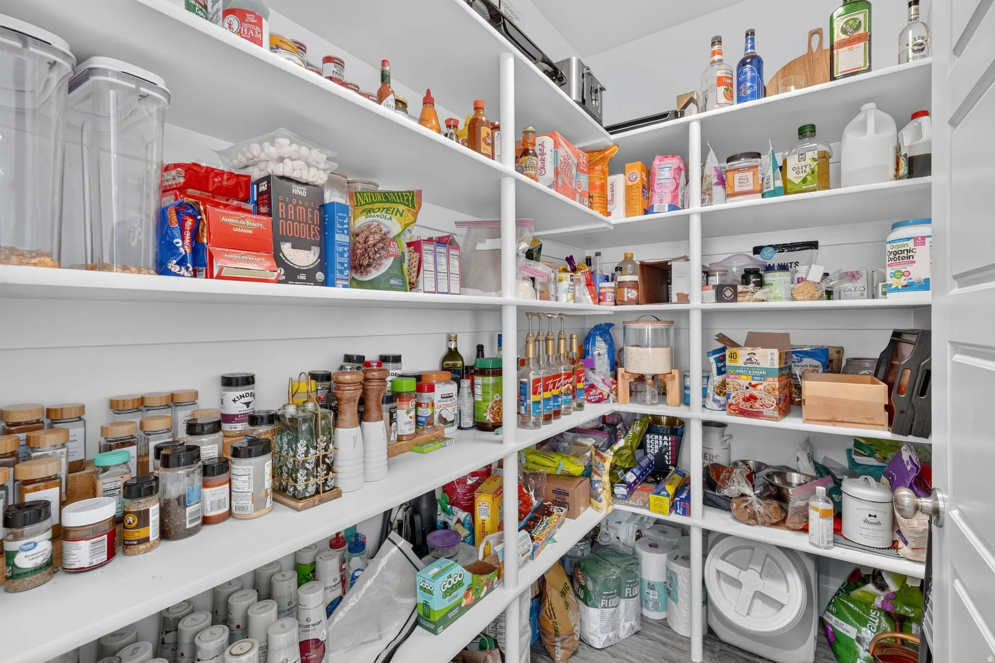 Expansive walk-in pantry featuring multiple levels of white shelving, plank-style wall paneling, and a light-colored flooring