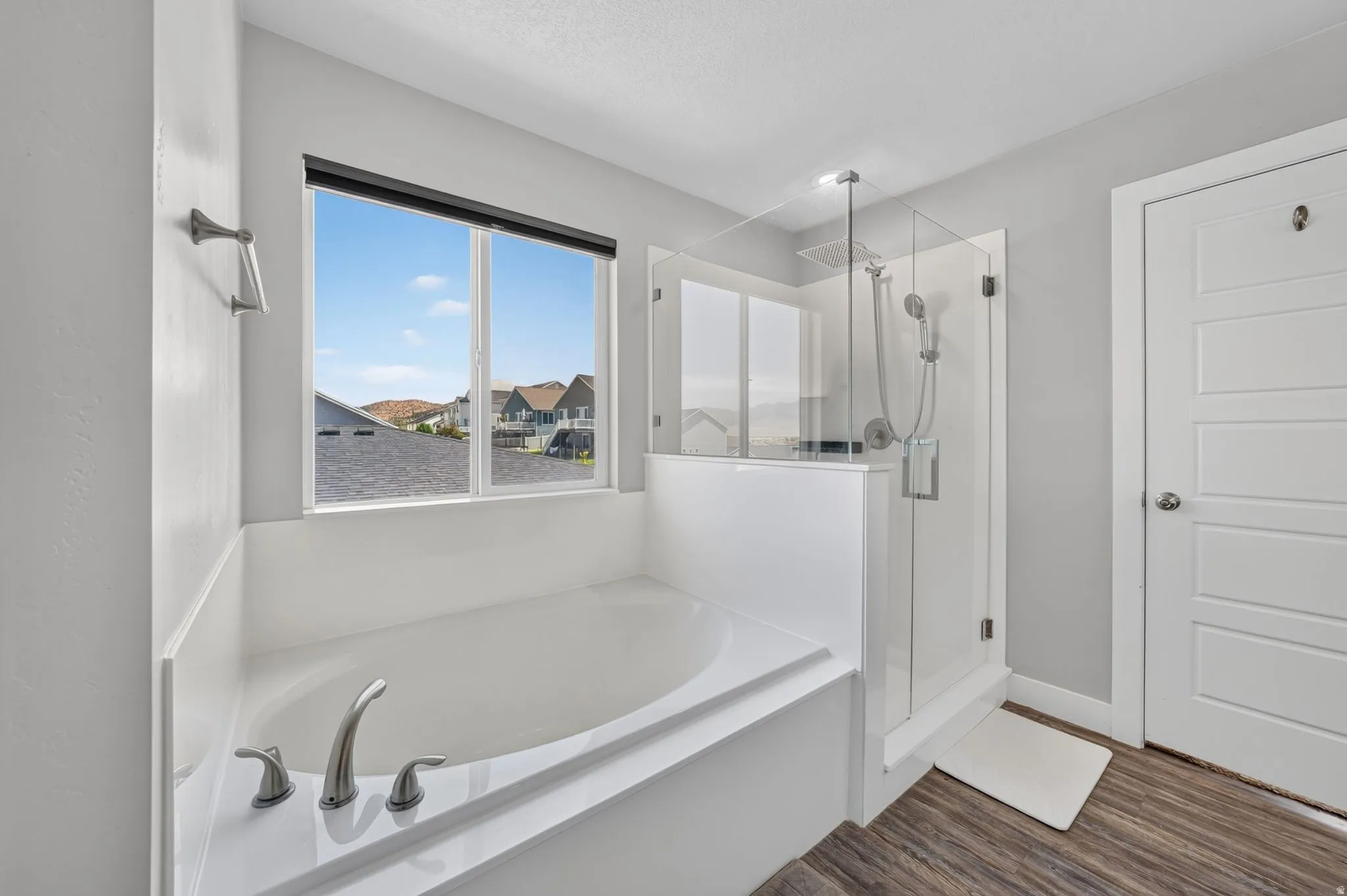 Soaking tub with brushed nickel fixtures, expansive window, clear glass shower enclosure with rain shower head, and wood-finish flooring