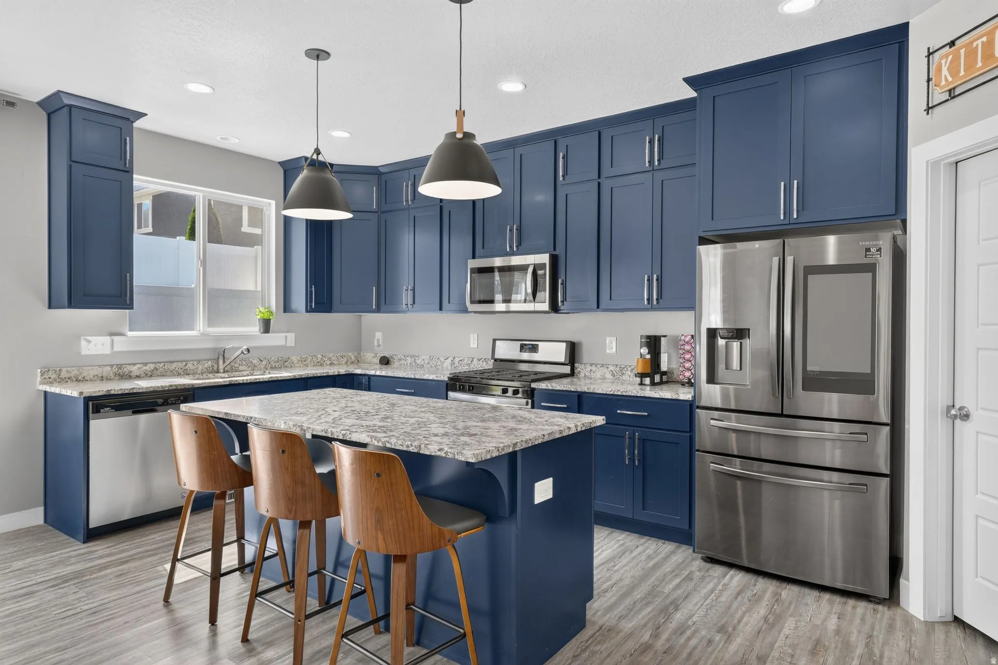 Kitchen featuring blue cabinetry, light-toned speckled countertops, and stainless steel appliances