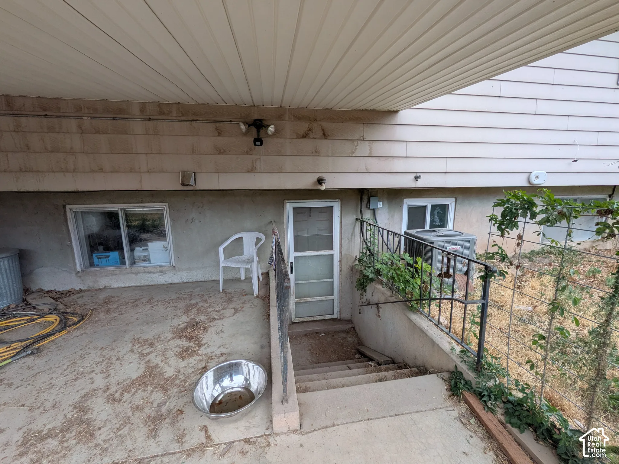 Lower-level exterior featuring a covered patio, concrete steps with metal railings, and dual-pane windows