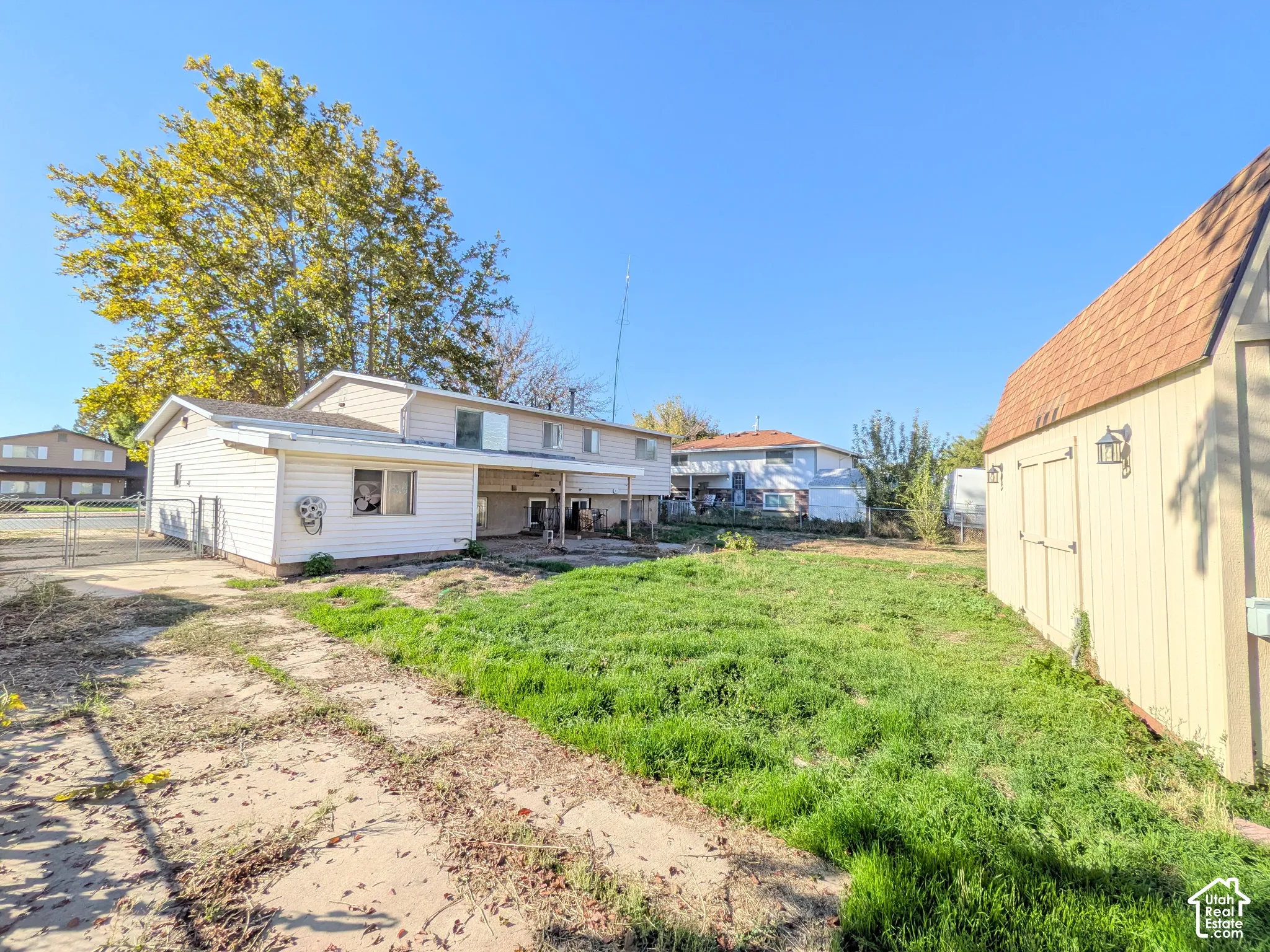 Expansive backyard featuring a large shed with exterior lighting, a two-story residence with light-toned siding, and a paved drive