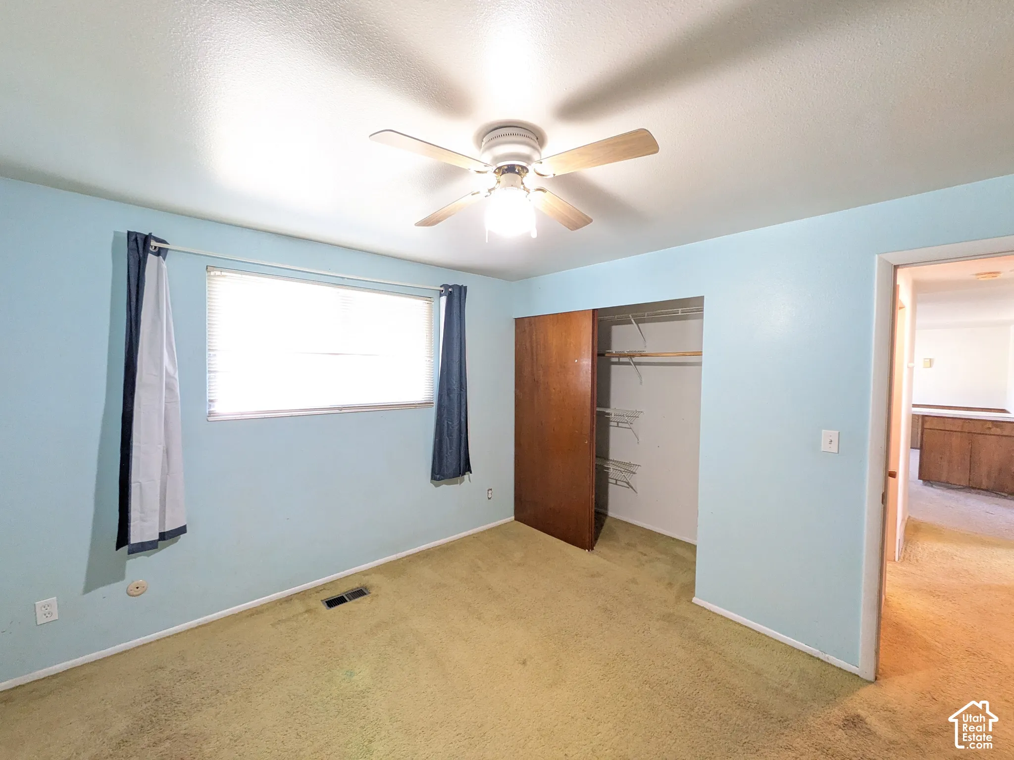 Recessed window with blinds, ceiling fan with integrated lighting, wood-finish closet doors, and light blue wall color