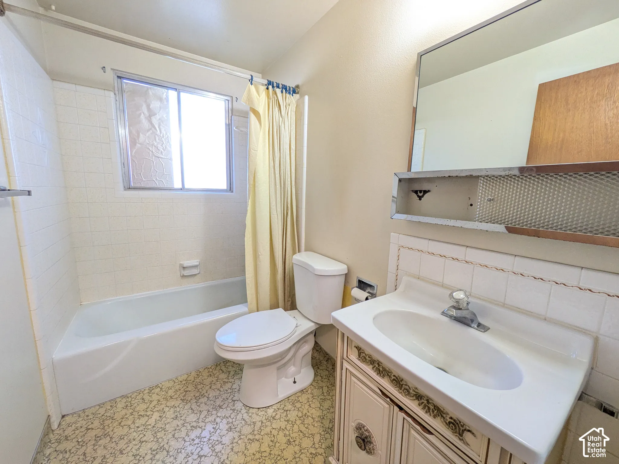 White bathtub with a window, white toilet, and a vanity with an integrated sink